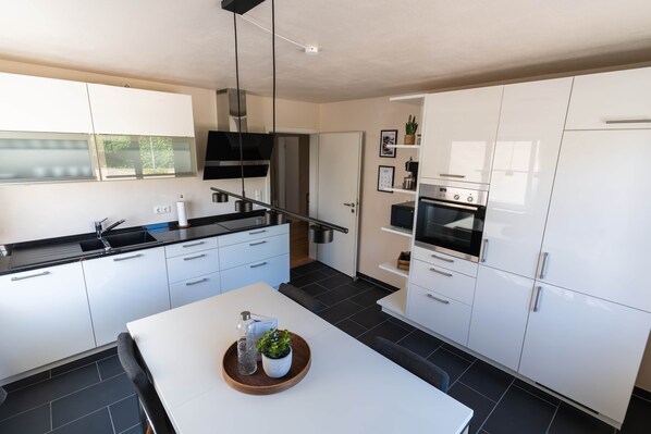 A modern kitchen with white cabinetry, a black countertop, and a dining area with a table.