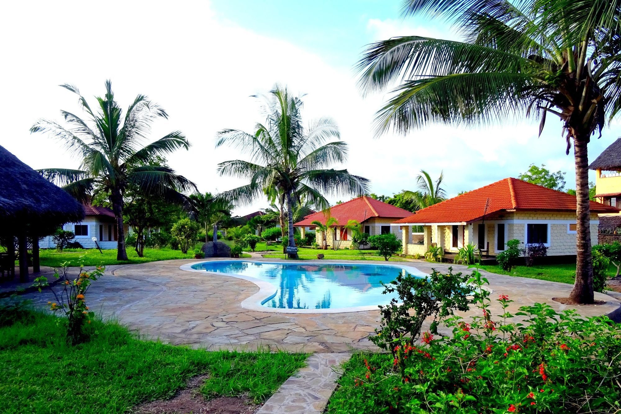 A resort with a swimming pool, palm trees, and thatched-roof buildings.