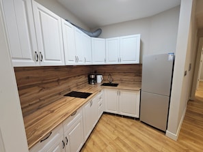 A compact kitchen with white cabinets, a wooden countertop, a coffee maker, and a refrigerator. - Stylish 2BR Apartment at Gerlug Vista with Skyline Views (Ulaanbaatar)