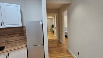 A modern kitchen with white cabinets, a refrigerator, and a wooden countertop.