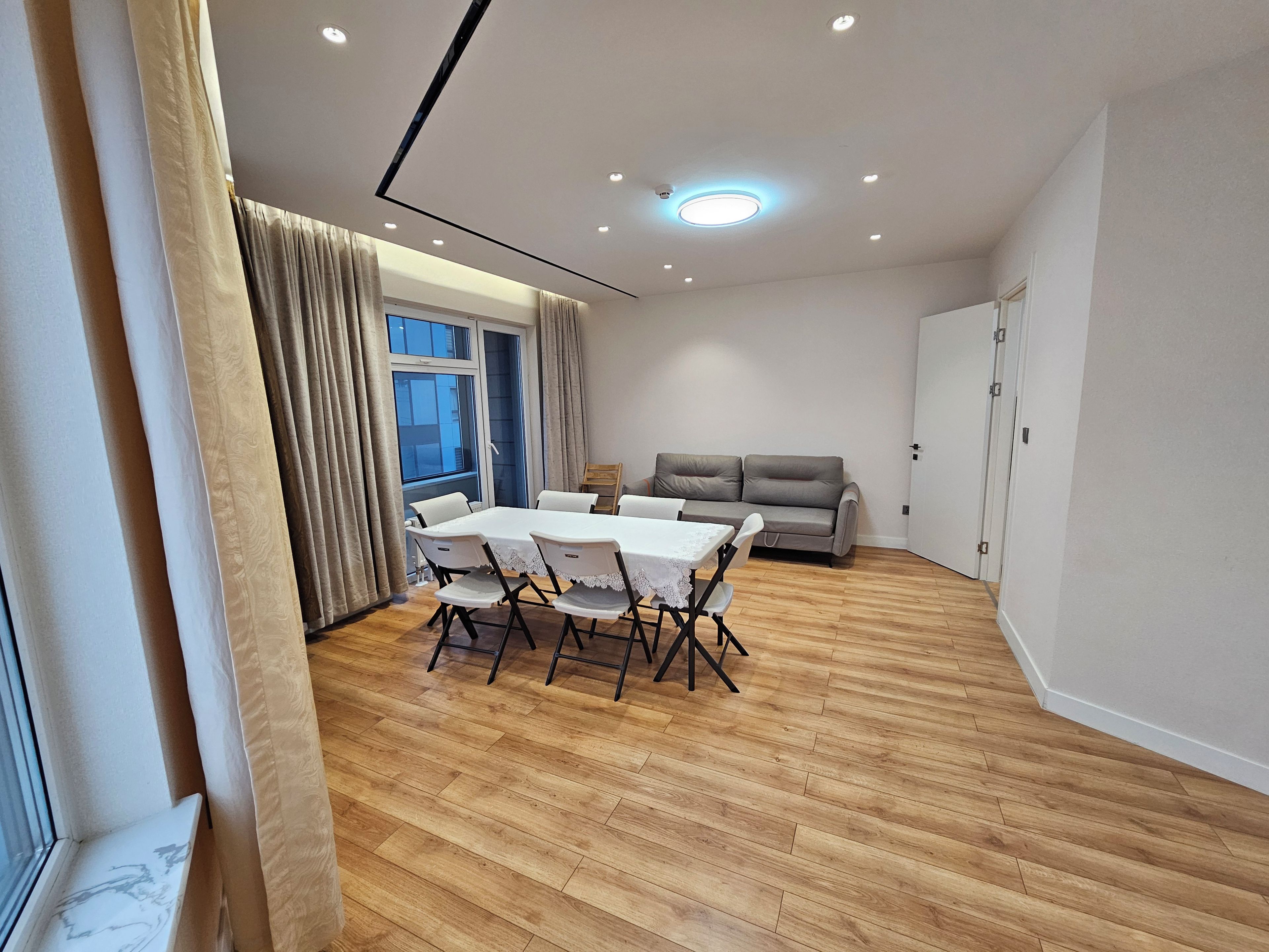 Una sala de estar moderna con una mesa de comedor, sofá y un ventanal grande.