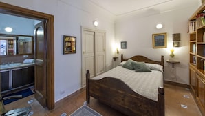 A bedroom with a wooden bed, a bedside table with a lamp, a bookshelf, and a door leading to another room. - Villa Deli (Positano)