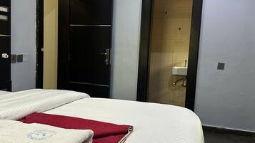 Habitación de hotel con una cama, una toalla roja y blanca, un armario y una puerta que da a un baño.