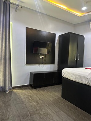 A modern bedroom with a bed, a wardrobe, a TV mounted on the wall, and a wooden floor.
