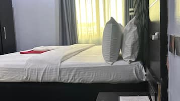Habitación de hotel con cama, mesita de noche, unidad de aire acondicionado y ventana con cortinas.