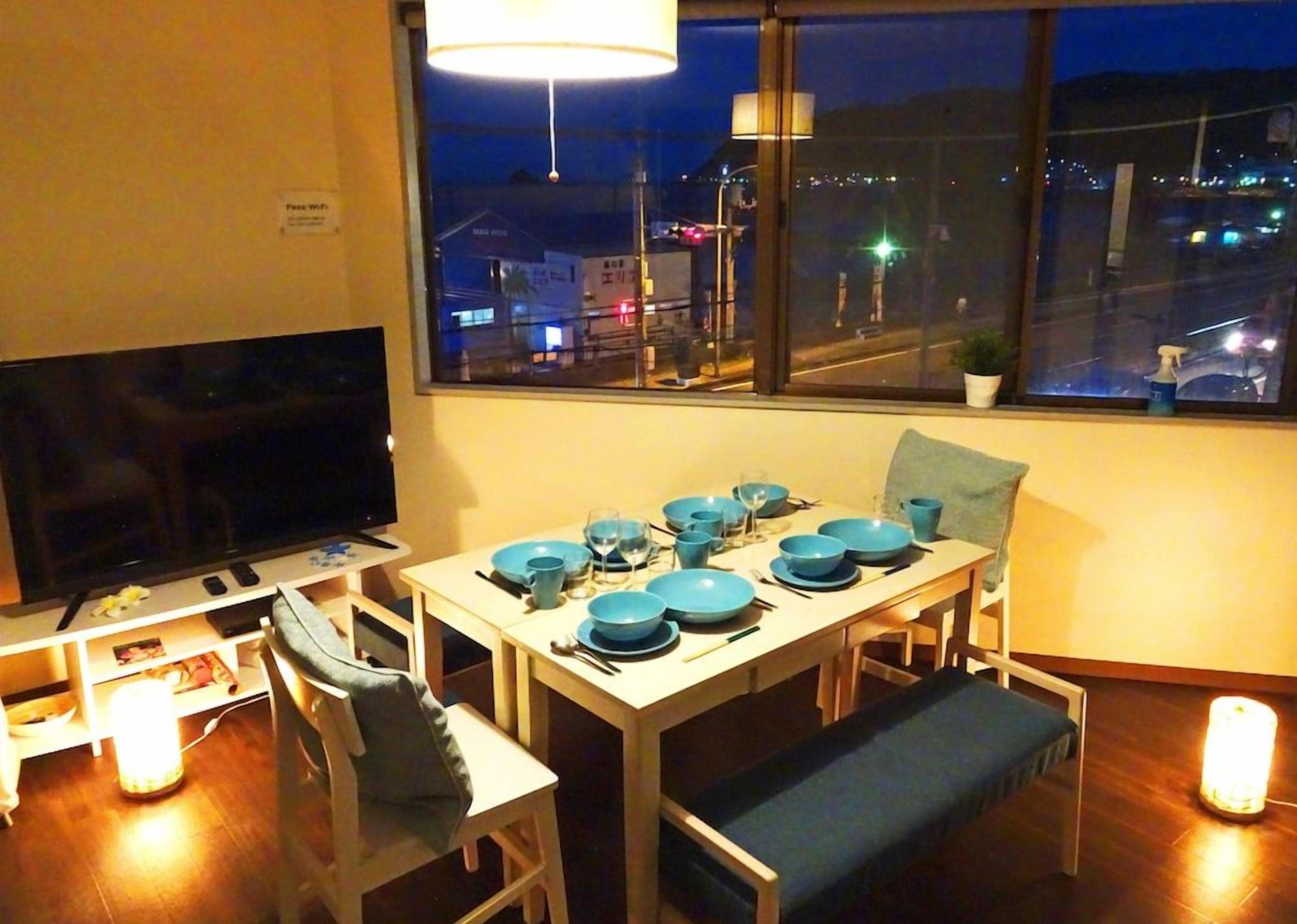 A dining area with a TV, table set with blue plates, and a city view through the window.