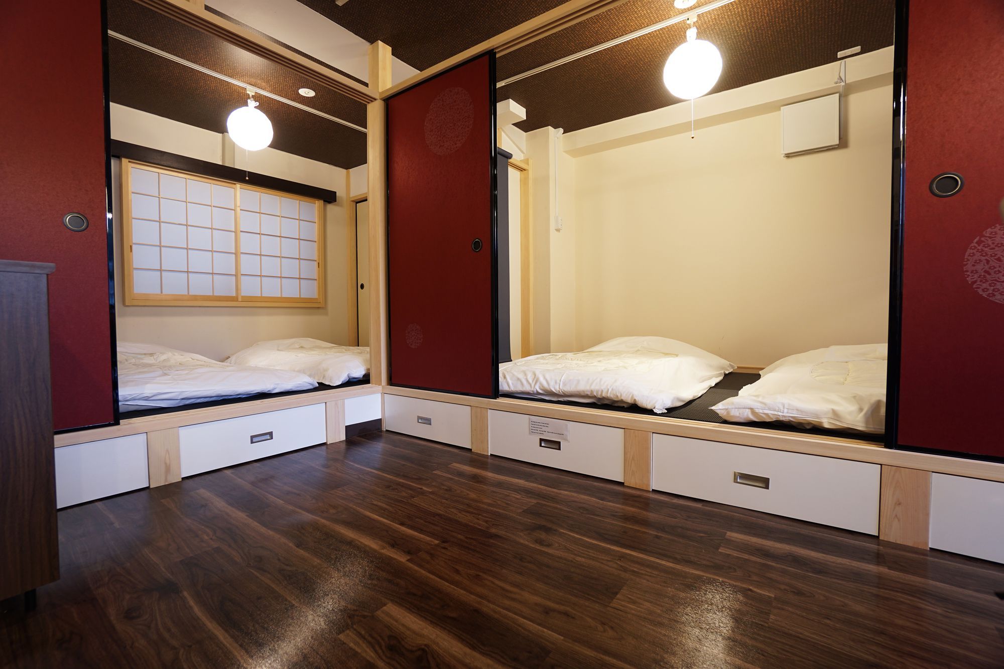 A hotel room with two beds, a wooden floor, and a traditional Japanese shoji screen.