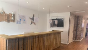 Zona de recepción con mostrador de madera, panel informativo en la pared y ventana con vistas al exterior.