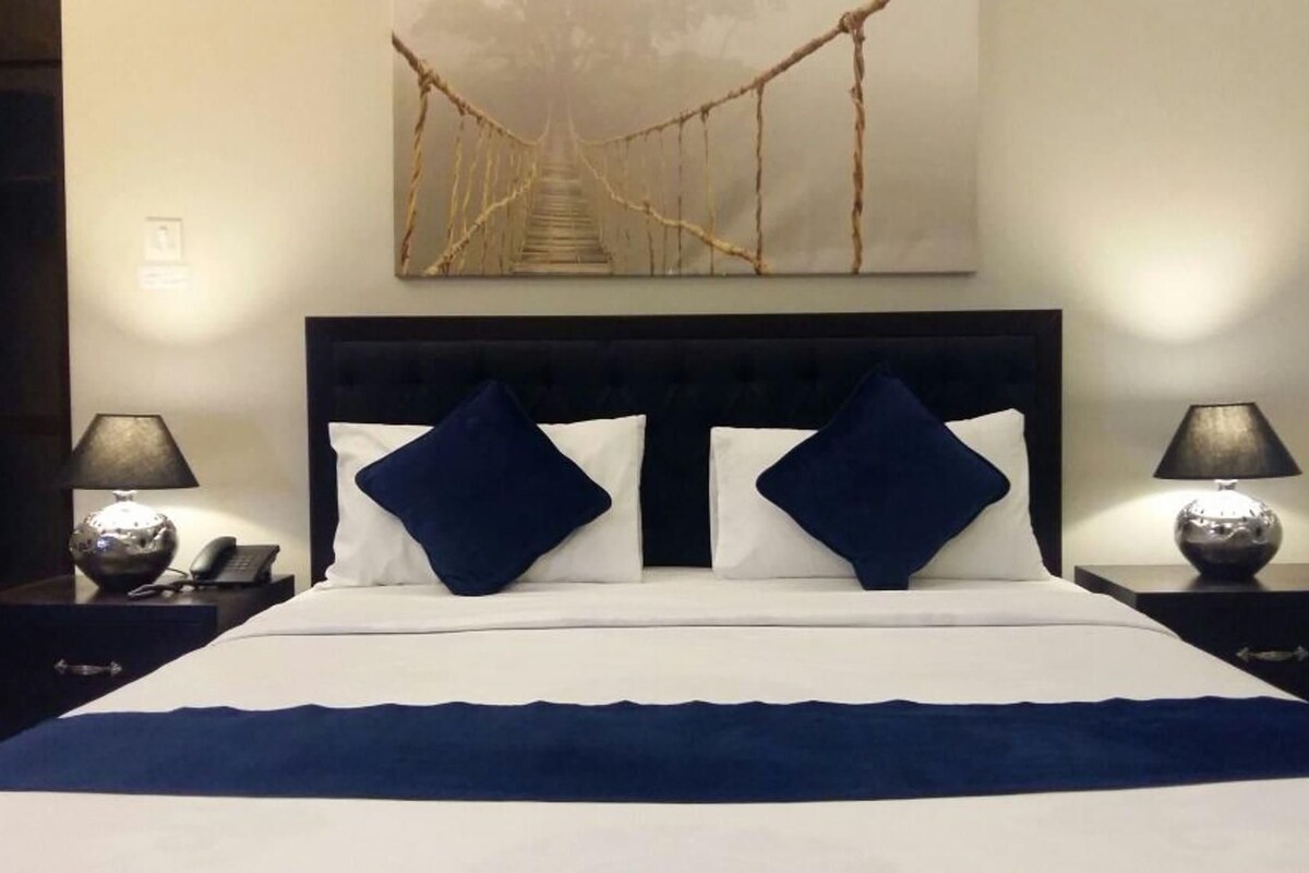 A hotel room with a bed, two nightstands, two lamps, a wall-mounted artwork, and a door.