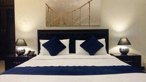 A hotel room with a bed, two nightstands, two lamps, a wall-mounted artwork, and a door. - Serene Residence (Islamabad)