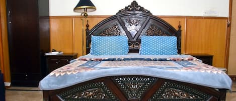 A bedroom with a wooden bed, two pillows, a nightstand, a lamp, and a wardrobe.