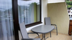 A balcony with a round table and two chairs, a window with curtains, and a textured wall. - Apartment Elisa (Kaprun)