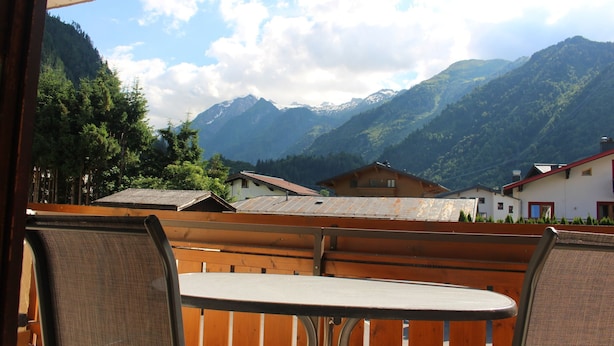 A view from a balcony with a table and chairs, overlooking a mountainous landscape with houses and trees. - Apartment Elisa (Kaprun)