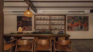 A dining area with a wooden table, chairs, a hanging light fixture, and a wall display of plates.