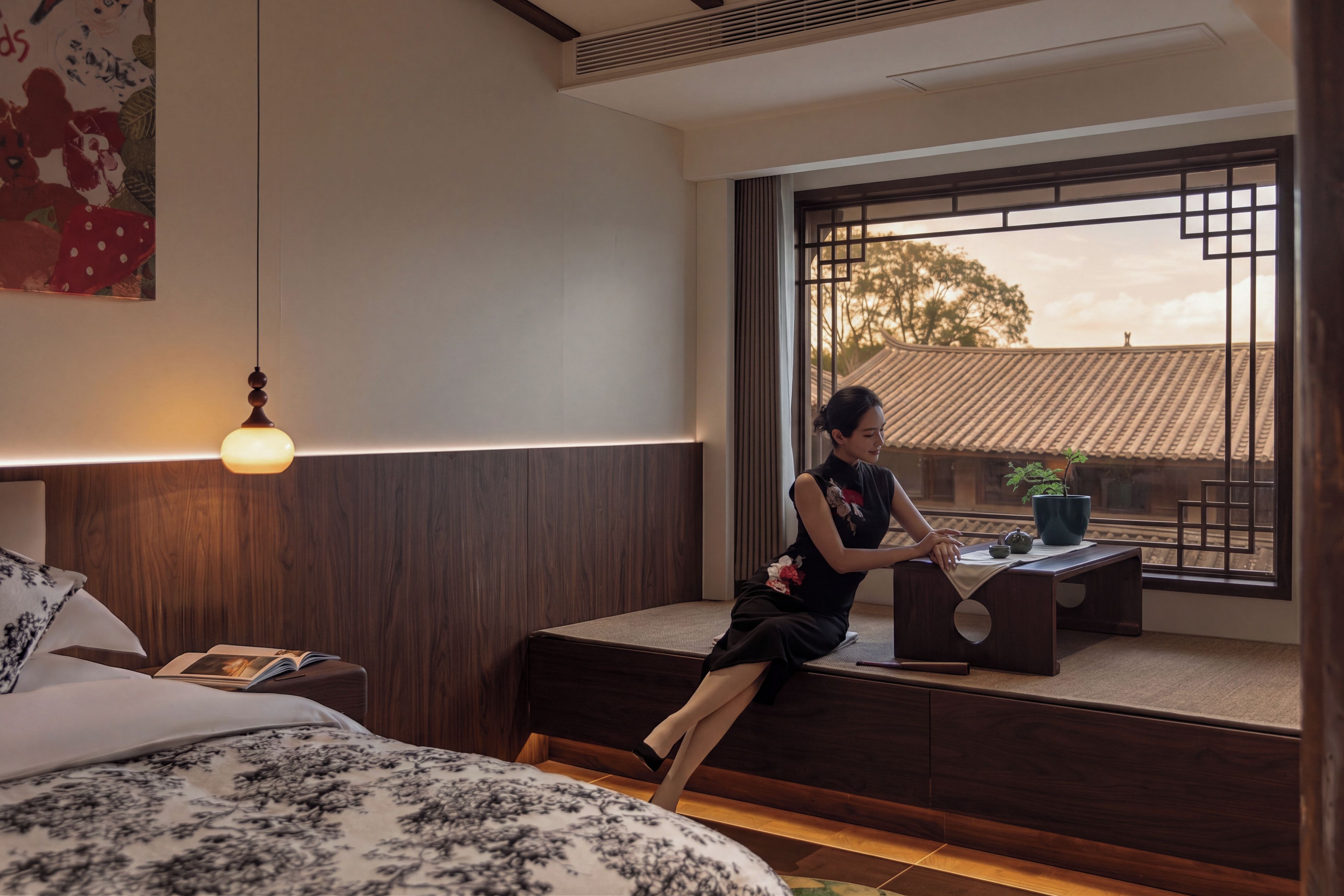 A room with a bed, a nightstand, a desk, and a window with a view of traditional architecture.