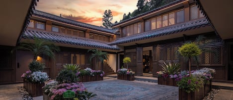 A traditional courtyard with wooden buildings, a central garden area, and a view of the sky.