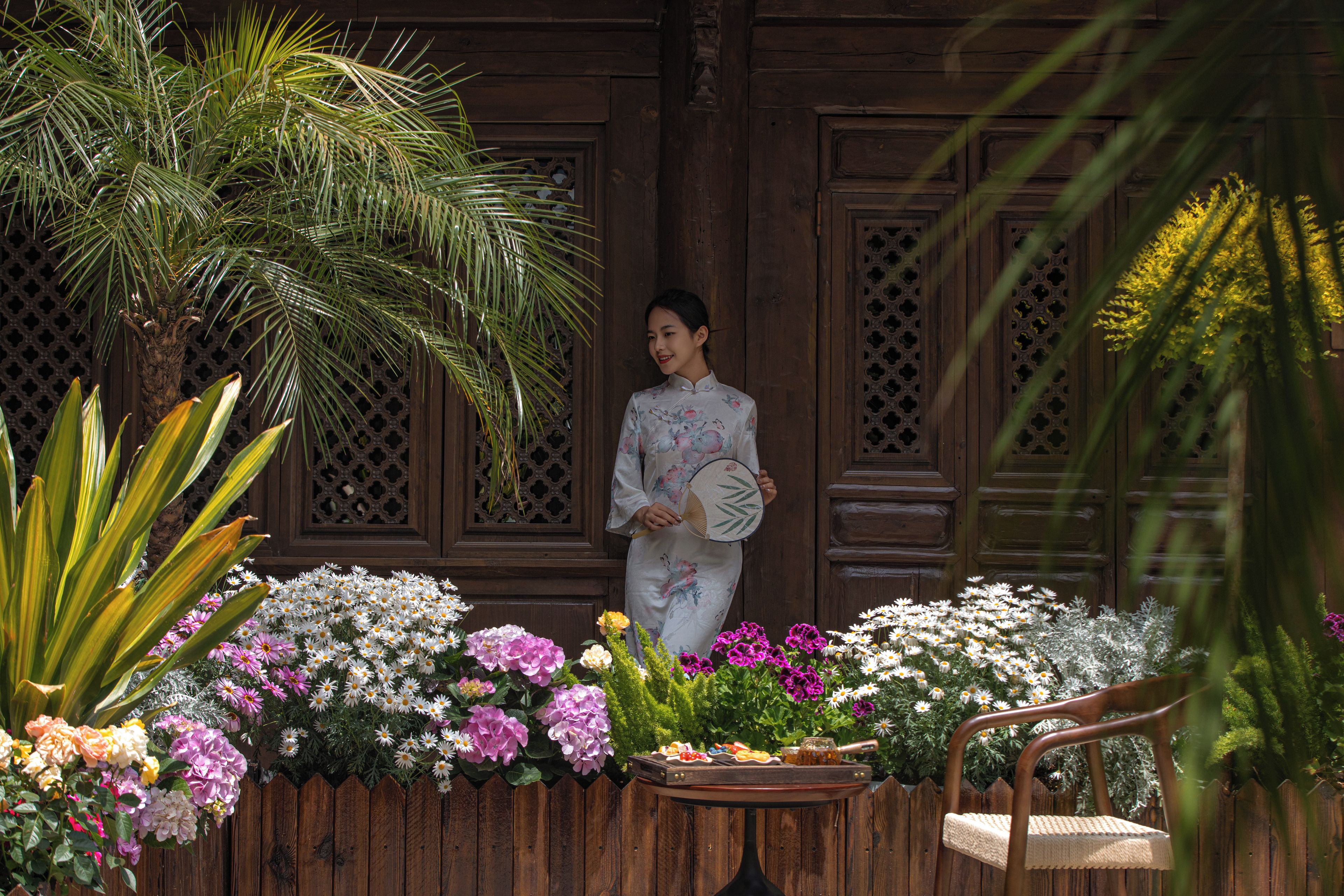 A person standing in front of a wooden structure with intricate carvings, holding a fan.