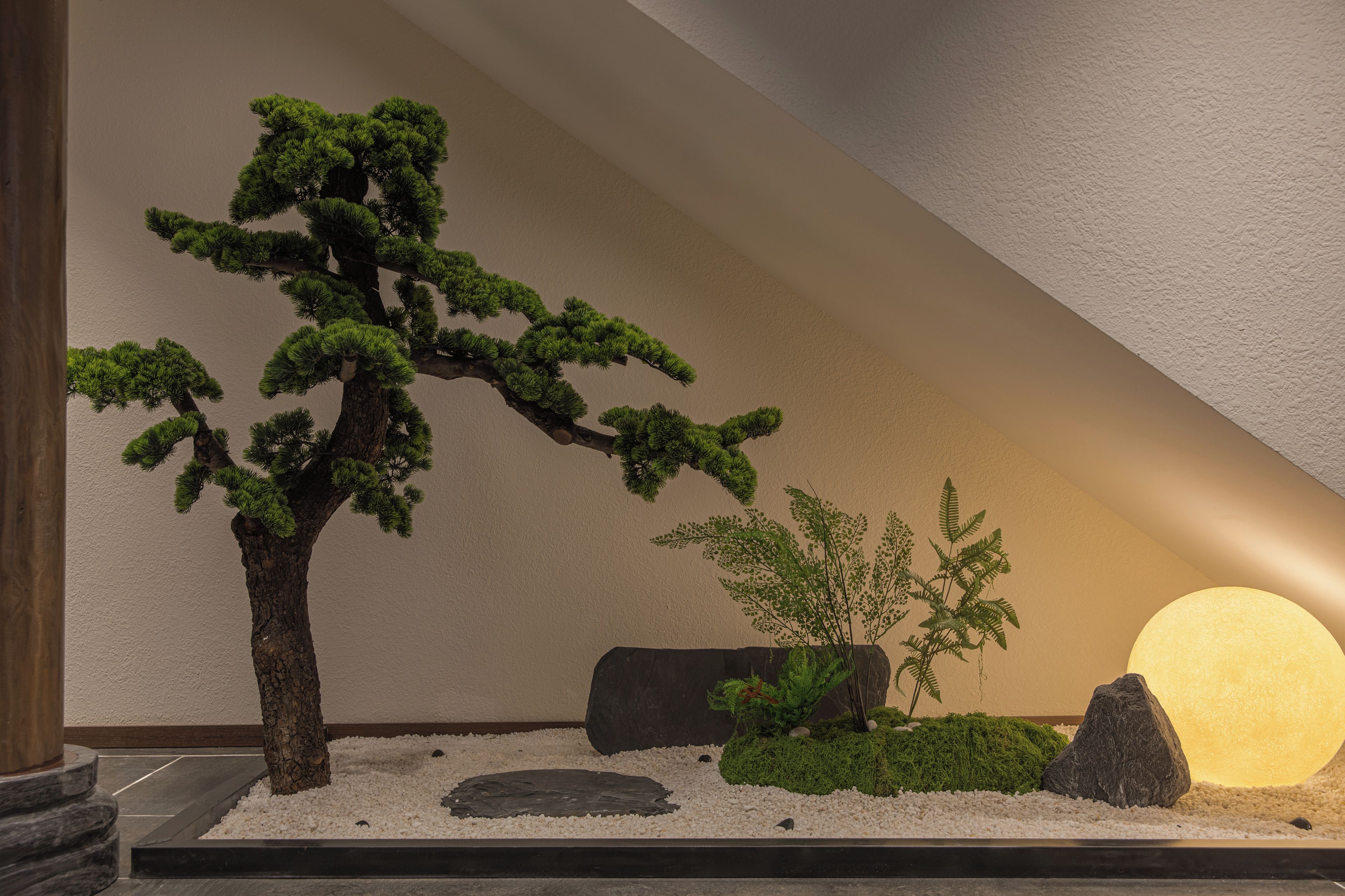 A zen garden with a bonsai tree, rocks, and a spherical light fixture.