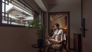 A room with a traditional Japanese-style interior, a potted plant, and a view of traditional buildings outside.