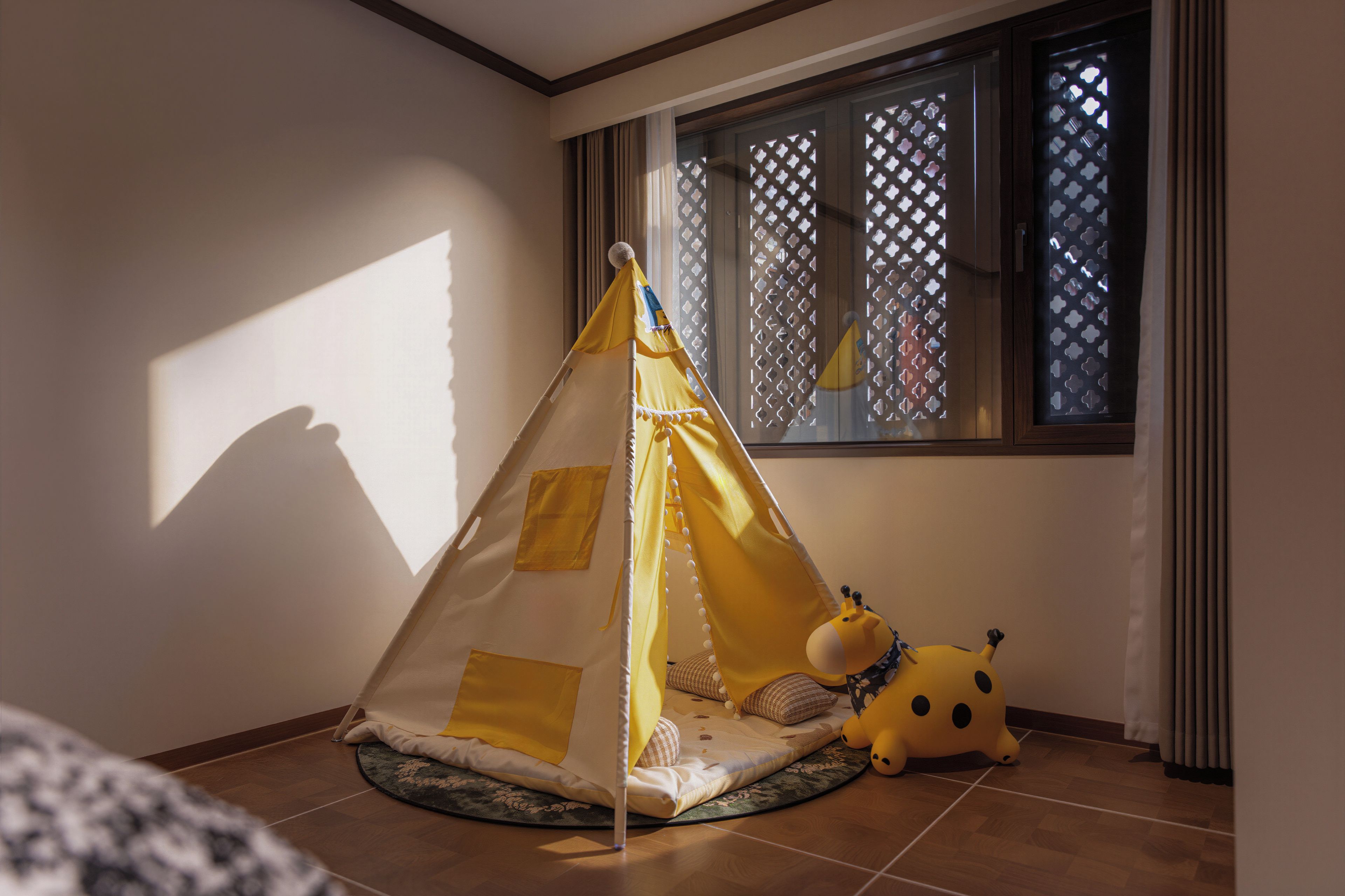 Una habitación con una zona de juegos tipo tienda de campaña, una ventana con persianas decoradas y un peluche en el suelo.