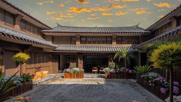 A traditional courtyard with tiled roofs, wooden structures, and a central seating area surrounded by potted plants and flowers.
