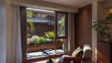 A room with a sliding glass door leading to an outdoor garden area, a wooden chair with a cushion, and a small table with a book.