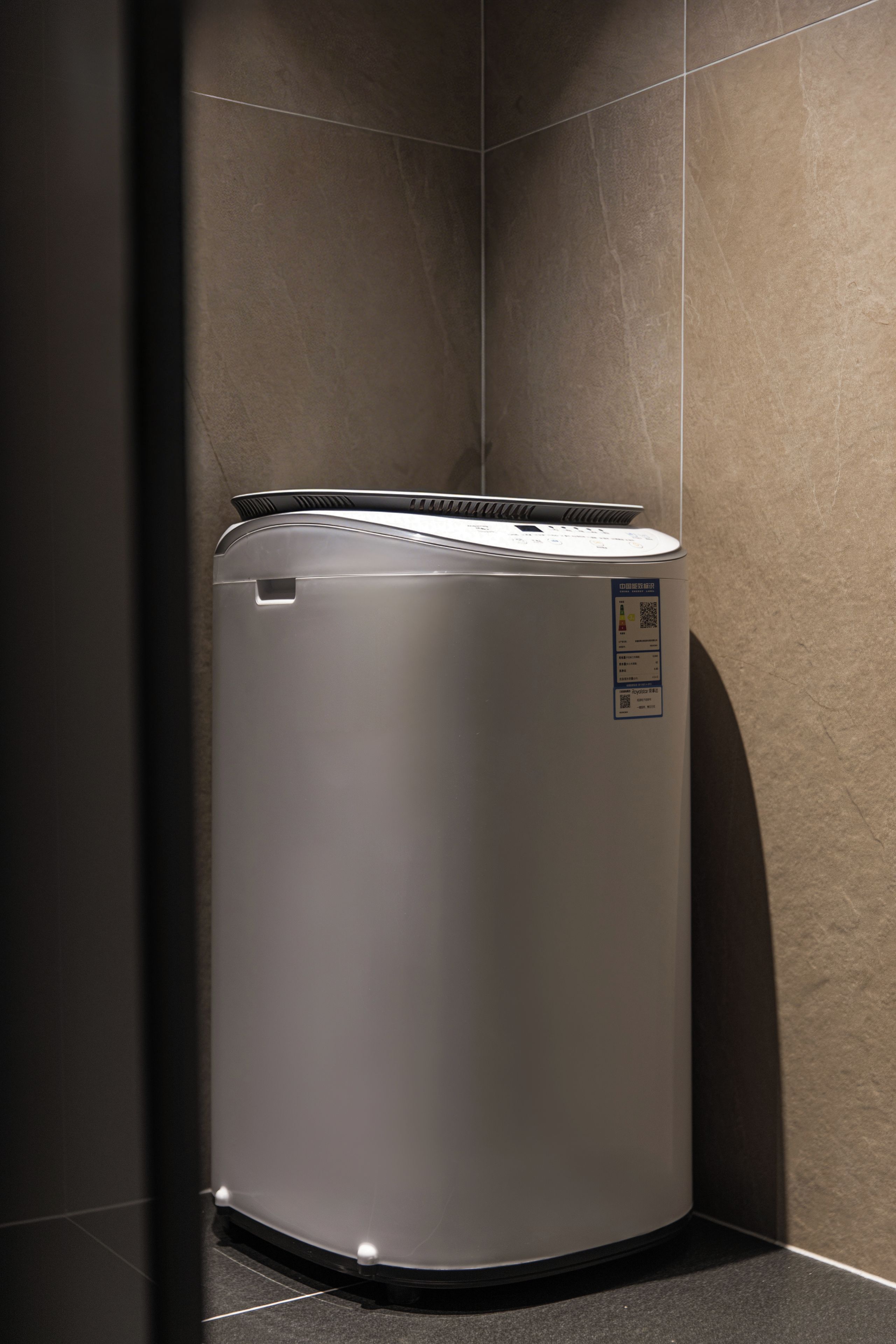 Un lave-linge compact et moderne, placé dans un coin d’une pièce dont les murs sont recouverts de carreaux.