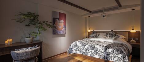 A bedroom with a bed, bedside table, chair, and a wall-mounted artwork.