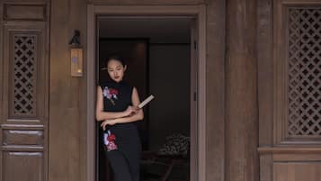 Une porte en bois ornée de sculptures complexes, une petite lampe fixée au mur et une personne tenant un livre.