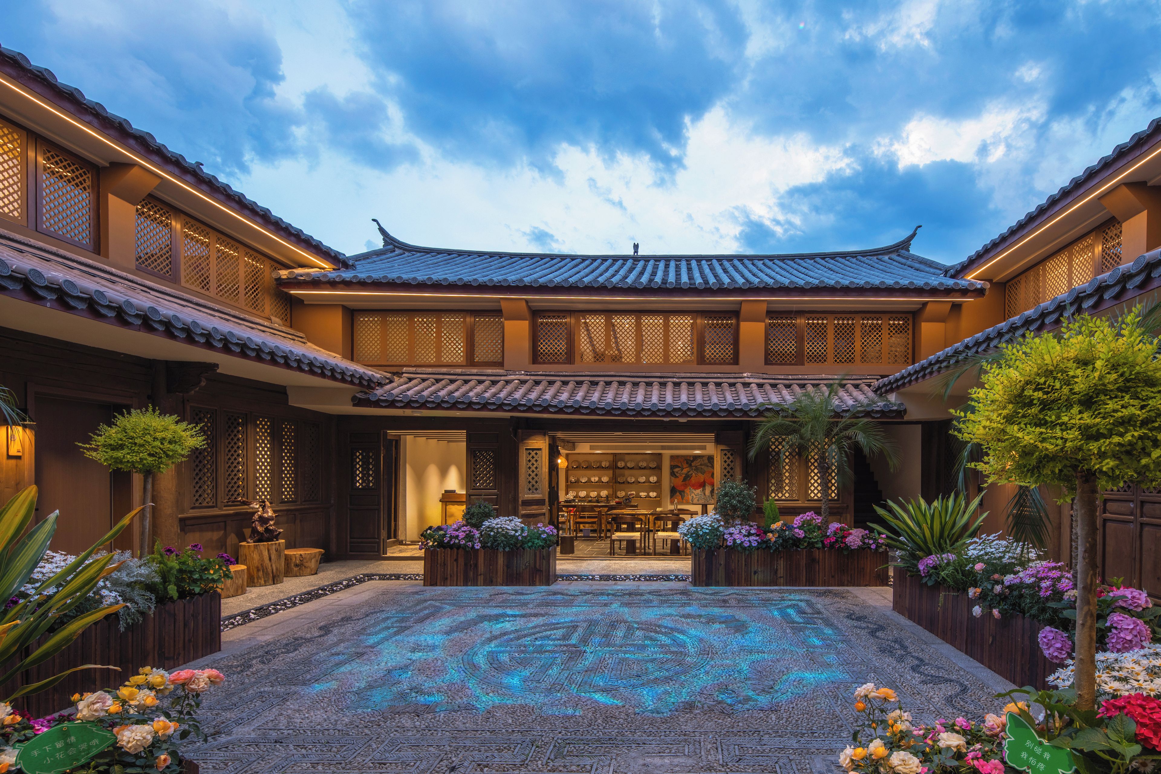 A traditional courtyard with a tiled roof, wooden lattice windows, and a central seating area with tables and chairs.