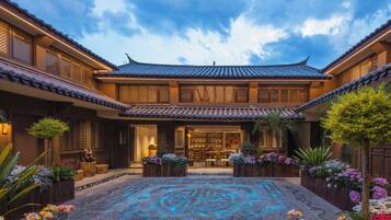 A traditional courtyard with a tiled roof, wooden lattice windows, and a central seating area with tables and chairs.