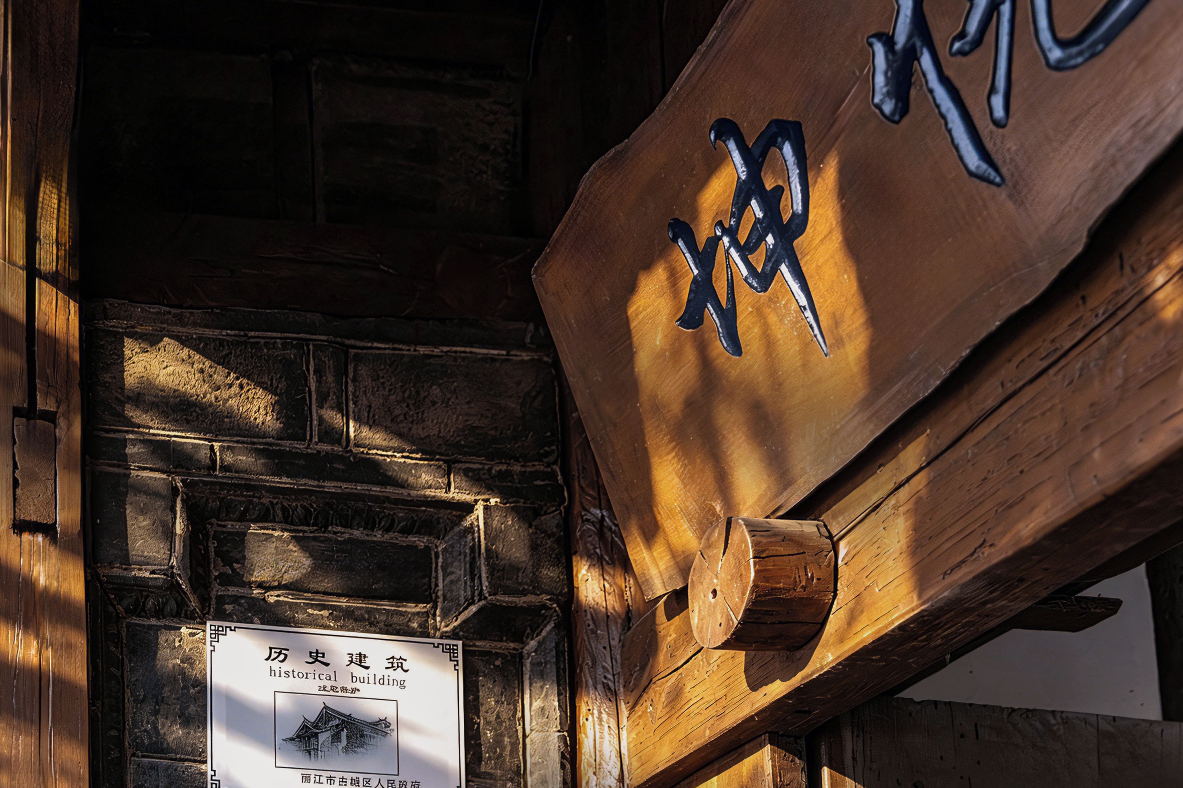A wooden sign with a traditional Chinese character and a plaque with a building's name and a small illustration.