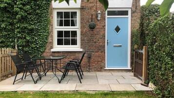 A brick house with a blue door, a white window, and a small garden with a table and chairs.