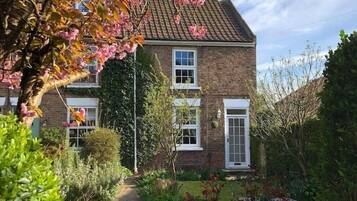 A two-story brick house with a visible front garden and a white fence.