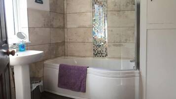 A bathroom with a white pedestal sink, a glass-enclosed shower, and a purple towel on the tub.