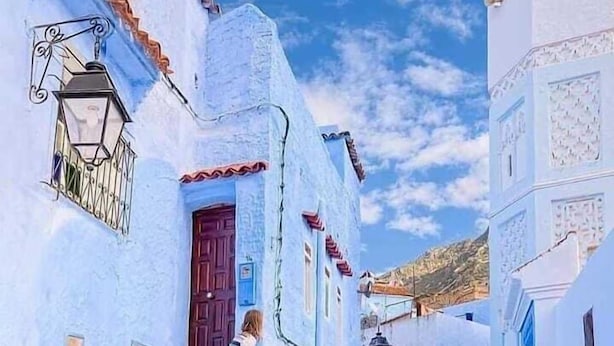 A narrow street with buildings painted in blue and white, a woman descending stairs, and a clear sky. - Casa Meryem (Chefchaouen)