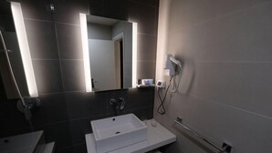Ein modernes Badezimmer mit einem weißen Waschbecken, einem Spiegel und einem an der Wand befestigten Fön.