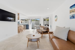 A modern living room with a sofa, a round coffee table, and a TV mounted on the wall. - "Leanda Sea Breeze"- Short walk to beaches & shops (Port Macquarie)