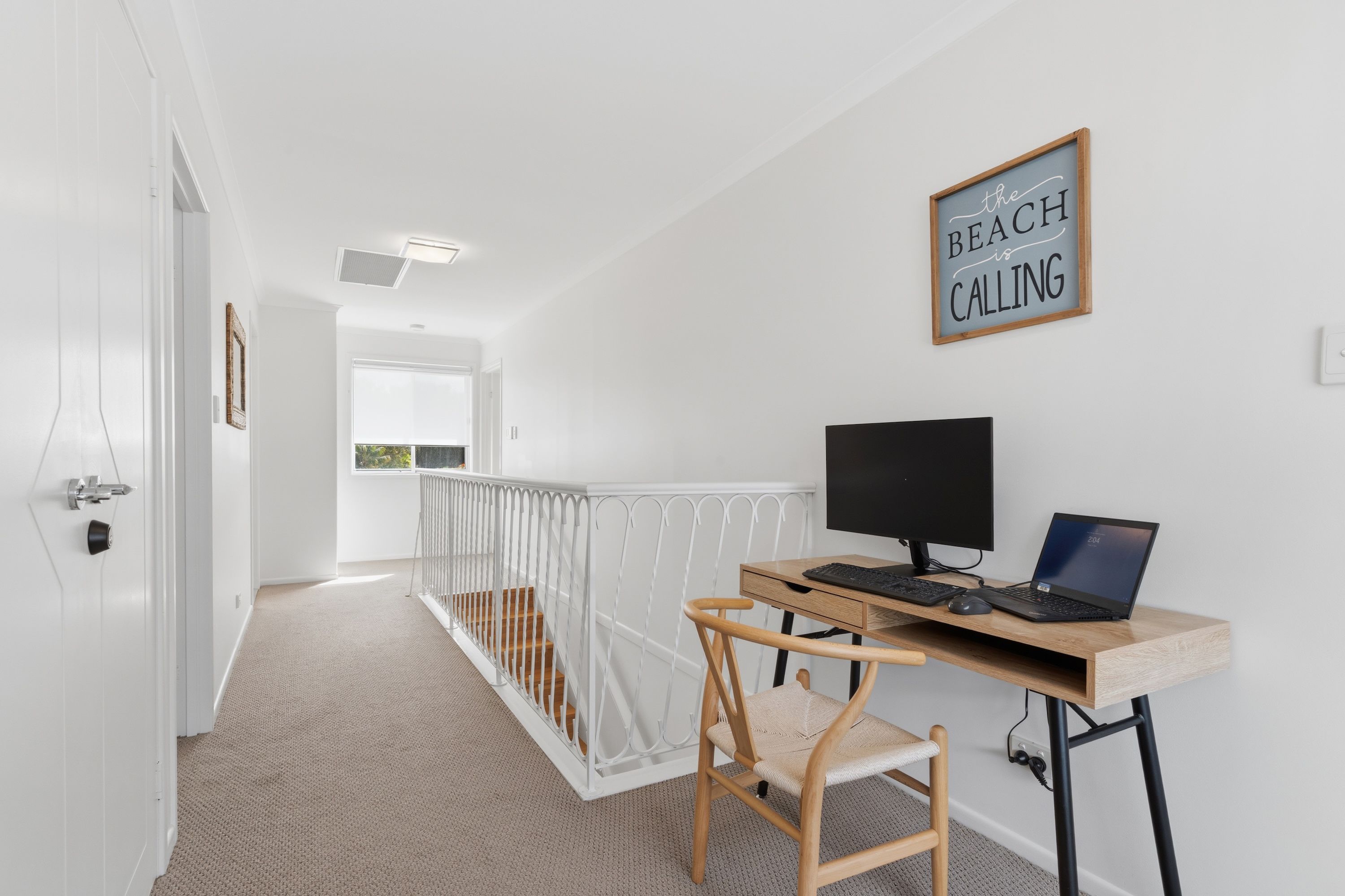 A modern room with a desk, computer, and a chair. There is a sign on the wall and a window with a view.