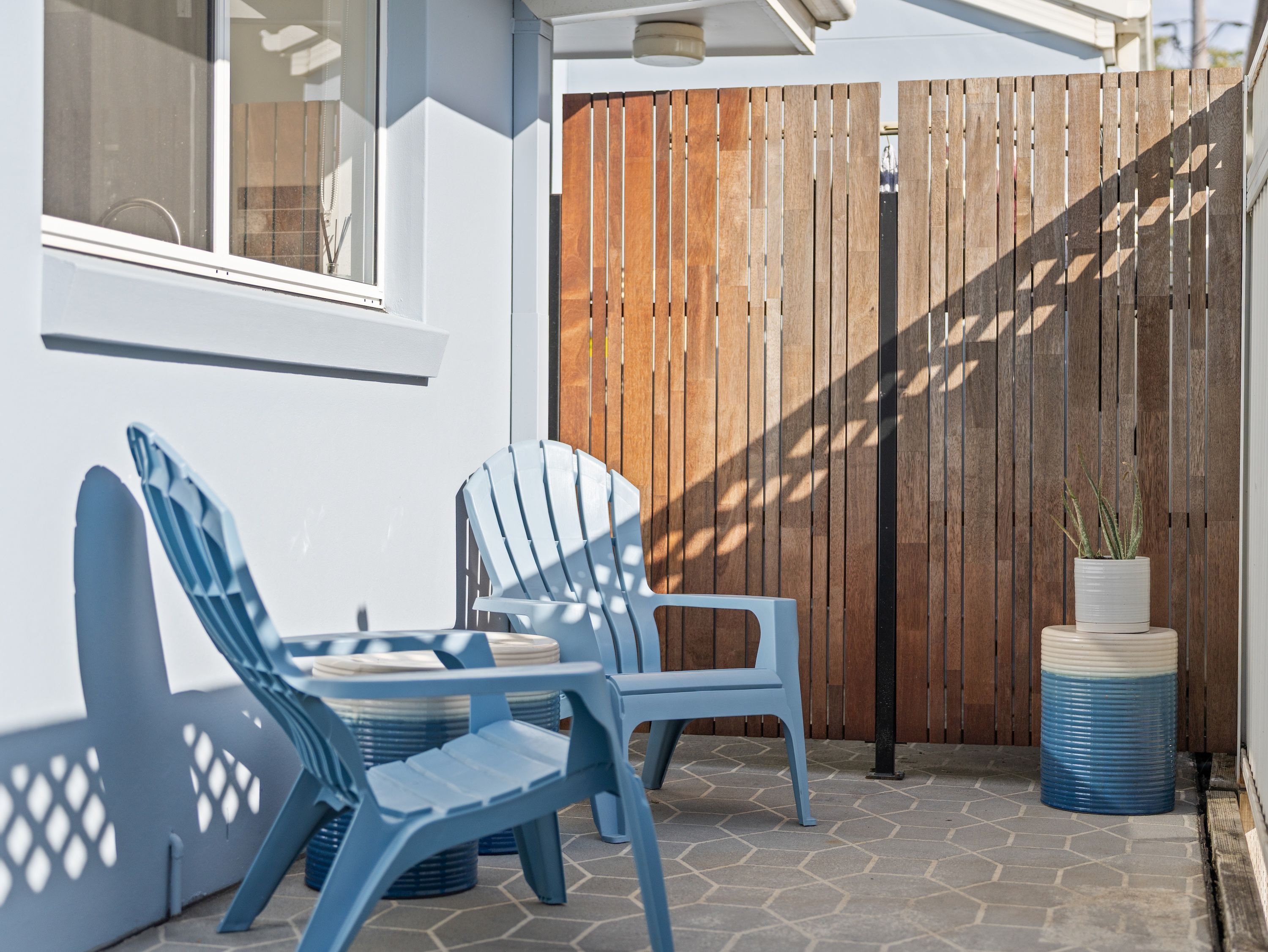 Een terras met twee blauwe stoelen, een houten hek en een bloempot.