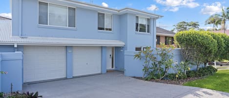 A two-story residential building with a garage, a covered driveway, and a well-maintained lawn.