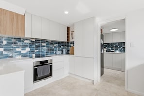A modern kitchen with white cabinets, a tiled backsplash, and a built-in oven. - "Leanda Sea Breeze"- Short walk to beaches & shops (Port Macquarie)