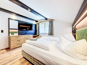 A modern bedroom with a large bed, a dresser, a television, and a window with curtains. - Chalet Jana by Interhome (Feichten im Kaunertal)