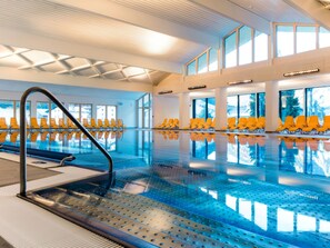 Ein Hallenbad mit gelben Stühlen und freiem Blick ins Freie durch große Fenster.