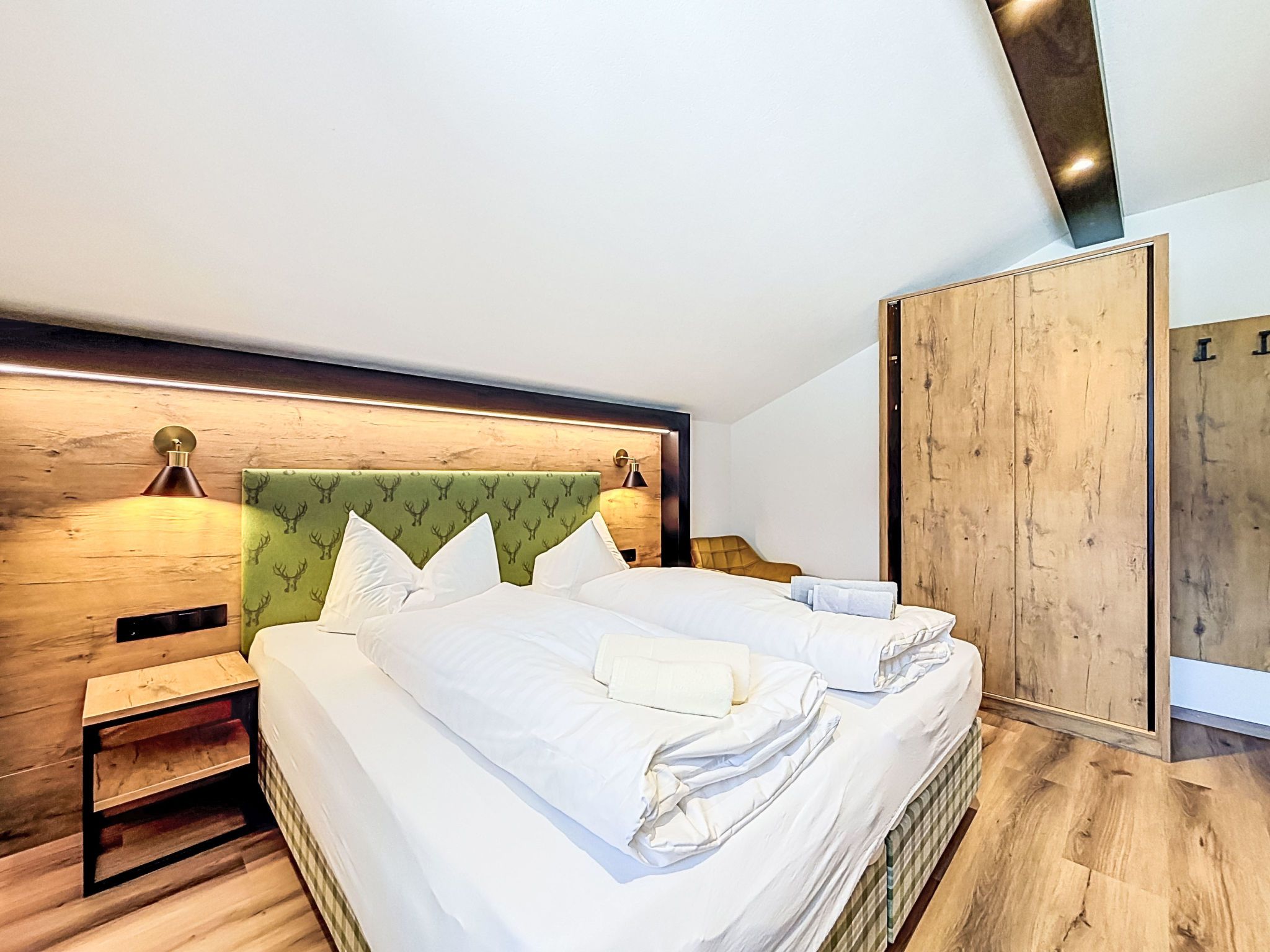 Ett modernt hotellrum med en stor säng, ett träpanelat sänggavel och en trägarderob.