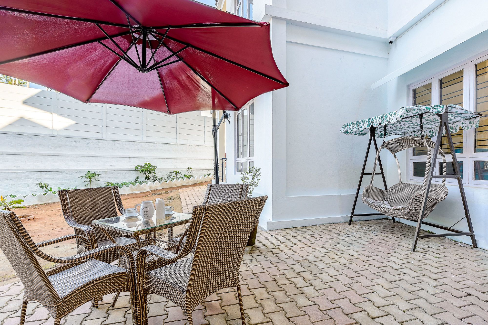 A patio area with wicker furniture, a red umbrella, and a hanging swing chair.