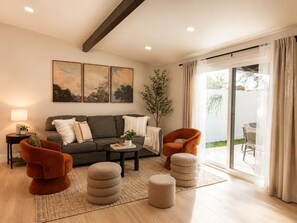 A modern living room with a sofa, armchairs, ottomans, a coffee table, and artwork on the wall. - Modern & Spacious Anaheim Home 7 Min to Disneyland Game Room Theater Sleeps 14 (Anaheim)