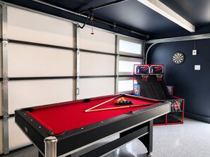 A pool table with a red felt surface, a dartboard, and two basketball hoops against a dark wall. - Modern & Spacious Anaheim Home 7 Min to Disneyland Game Room Theater Sleeps 14 (Anaheim)