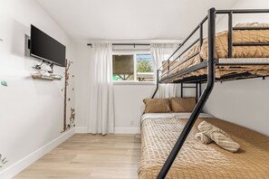 A bunk bed room with a TV mounted on the wall, a window with curtains, and a small shelf with books. - Modern & Spacious Anaheim Home 7 Min to Disneyland Game Room Theater Sleeps 14 (Anaheim)