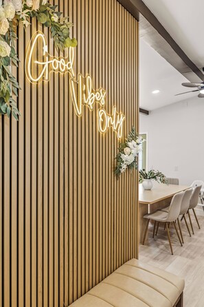 A modern interior with a wooden slat wall, a neon sign reading 'Good Vibes Only', a dining area with a white table and chairs, and a bench. - Modern & Spacious Anaheim Home 7 Min to Disneyland Game Room Theater Sleeps 14 (Anaheim)